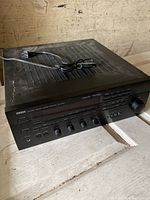 Photo showing a black Yamaha stereo receiver with control knobs, buttons, headphone jack, and power cord on top. Unit shows minor wear.