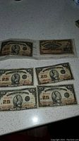 Six Dominion of Canada 25 cent banknotes laid out on a white speckled countertop, five from 1923 with Britannia design, one from 1900 with a distinct design, all used and worn.