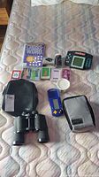 Overview of whole lot showing binoculars, handheld electronic games, bingo dabbers, playing cards, and poker chips on a mattress.