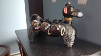 Full side view of black ceramic poodle decanter with 5 attached cups on its back.