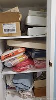 Three shelves filled with folded fabric, sheets, and fabric remnants, visible packing materials and boxes.