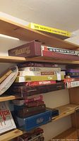 Shelf showing stacked vintage board games including Trivial Pursuit, Spirograph, Monopoly, Password, and other boxed games.