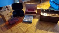 Photo showing all seven jewelry boxes arranged on the floor from a slight angle, including wooden, plastic, and acrylic styles with multiple compartments.