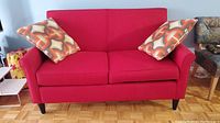 Front view of red loveseat with two geometric patterned cushions, showing overall condition and style.