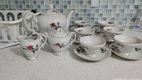 Photo of complete tea set showing white porcelain teapot, sugar bowl, creamer, and six cups with saucers all decorated with floral design and gold trim.