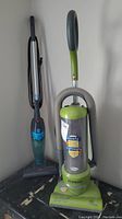Photo showing the Eureka EZ Clean upright vacuum in green with clear dust container and Bissell electric broom beside it.
