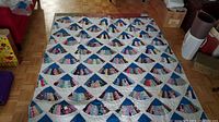 Full view of the quilt laid flat on a wooden floor, showing all the fan-shaped patchwork blocks and blue tops, overall pattern and condition.