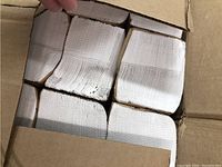 Top view showing packages of white singlefold paper towels inside an opened cardboard box.