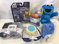 Photo showing the Cookie Monster plush toy, Paw Patrol Chase action figure with dog, a bucket of colorful plastic eggs, toddler socks, a toy wheel, and kids sunglasses.