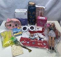 Full view of all items laid out including Barbie doll in bag, Hello Kitty poncho, mini fan, water bottle, cat purse, sunglasses, decorative key, and small toys.