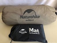 Photo of the two storage bags for a tent and mat showing Naturehike branding; beige bag for tent, black bag for mat.