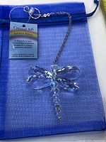 Crystal Art dragonfly suncatcher shown on blue organza pouch with product tag visible