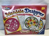 Front of sealed Ravensburger Mandala Designer Romantic art kit box showing title, recommended age, and illustration of stencil use and colored mandalas.