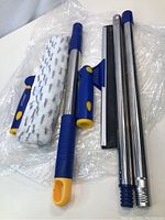 Photo of the disassembled window cleaning pole with roller brush, squeegee, and grip accessory on clear plastic sheet.