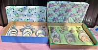 Two antique Japanese doll china sets in original cardboard boxes, displayed side by side showing contents and packaging