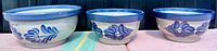 Front view showing three signed BBP salt glaze mixing bowls with blue flower decoration and blue rims.