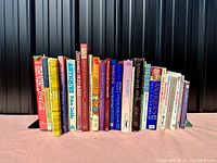 Photo of hardcover and paperback books standing vertically related to antiques and collectibles, showing varied sizes and colors with titles visible distinguishing their content.