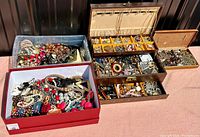 Three containers filled with mixed jewelry: two open boxes and one wooden jewelry box with trays