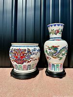 Two porcelain pieces displayed side by side, a planter and a vase on black stands, under natural light with vertical black background.