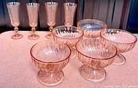 Four pink roslaine champagne flutes and five pink roslaine dessert bowls arranged on surface.