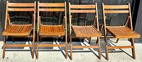 Front view of all four vintage folding wooden chairs aligned side by side outdoors, showing uniform polished wood finish and slatted seat design.