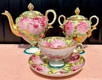 Partial tea set including teapot, covered sugar bowl, cup and saucer with bright pink floral design and gilded details on bone china.
