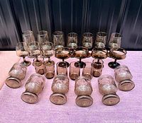 Front view of the full smoked glassware set arranged on pink cloth surface, showing all items including stemware and tumblers.