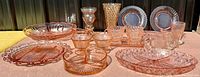 Wide view of diverse pink depression glass pieces arranged on a table showing plates, divided dishes, cups, vases, and serving dishes.