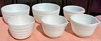 Seven vintage Pyrex milk glass mixing bowls in ribbed pattern, all arranged on table. Some have pour spouts visible.