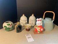 Full view of all seven Asian decor items including kabuki decanters, tea pot, cup, vase, figurine, and Buddha altar piece