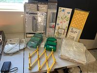 Photo of the entire collection: shoe organizers, garment bags with floral and yellow prints, chrome closet rod, clear suit covers, and sweater organizer on white table.