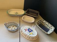 Six assorted European ceramic casserole and decorative dishes including oval lidded casserole, rectangular dishes with floral and geometric patterns, and a lattice open cut-out bowl.