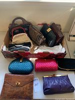 Box containing multiple clutch purses of various styles and materials including snake skin, woven, leather, and floral designs.
