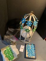 Full image of the white painted metal pendant lamp with cage and some attached blue and green metal flowers. Additional metal flowers shown in two separate boxes.