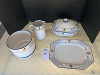 Four hand-painted Portuguese ceramic items: serving platter, covered casserole dish, plant pot with dish, and small pitcher, arranged on a table with black backdrop.