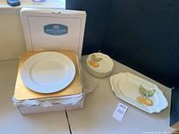 Photo showing Royal Gallery dinner plate chargers stacked on gold boards inside their box, and Villeroy & Boch Cascara dessert plates and serving platter with lemon design arranged nearby