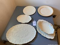 Full view of six assorted cream colored platters and bowls laid out on table showing sizes and shapes