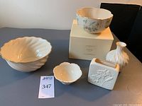 Five Lenox vases and bowls displayed on a table, showing various shapes and gold detailing, one item in box.