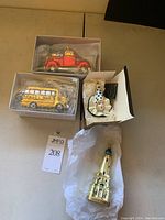 Four Christmas ornaments displayed together showing school bus, red truck with tree, sad clown face, and water tower.