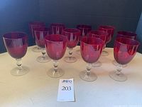Set of twelve ruby red glass goblets with clear glass pedestals and stems arranged in rows.