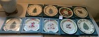 Nine Lenox Annual Holiday Collector Plates arranged on a table, showing varying designs including Christmas trees, Santa Claus, and holiday wreaths.