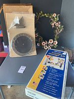 Photo showing all items: painted metal floral wreath, boxed sundial, Wood Logic garage storage kit box