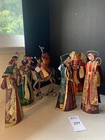 Seven handmade painted metal nativity scene figures including Mary, Joseph, the Angel, and the three Wisemen posed against black background and window light.