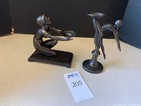 Pair of dark metal art deco style candle holders shaped as female figures, one kneeling and holding a dish, the other balancing on one leg, displayed side by side on a surface with a lot tag.