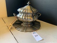 Pewter soup tureen with lid on scalloped serving tray showing front and side with two handles.