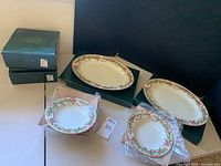 Two oblong serving platters alongside eight soup bowls, some still in packaging, with visible holly and red ribbon decorative patterns with gold edging on white fine china.