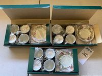 Three open boxes showing 12 demitasse cups and 12 matching saucers with festive holiday design.
