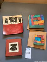 Overview photo showcasing four pieces of Sally Jaffee pottery art including two plates and two colorful tiles.