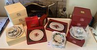 Overview of eight boxed 5-piece place settings in red and cream boxes with platters, mugs, bowls on table