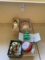 Five vintage mercury glass Christmas ornaments arranged with each in or near an open box, including two Santa heads, one Christmas tree, one Santa with wreath.